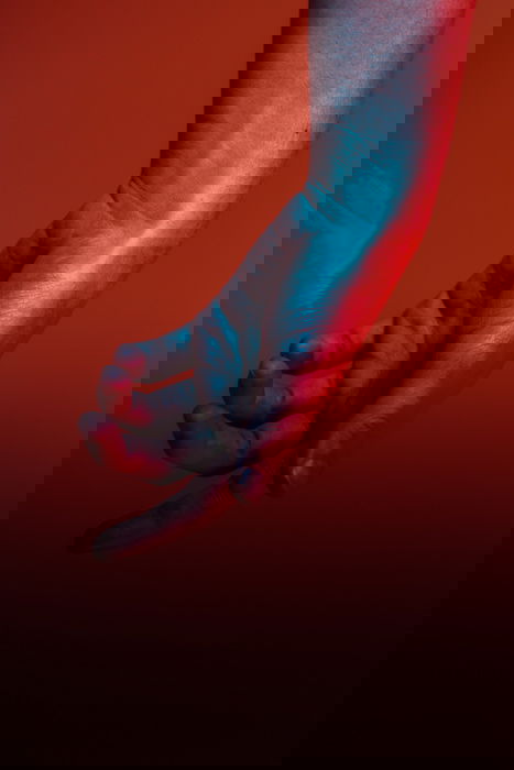 A blue and red toned hand against a red background 